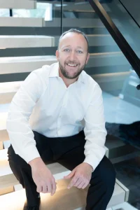 Josh Holt smiling photo sitting on stairs in white shirt